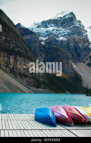 Colourful canoes lined up on a dock off a turquoise mountain lake  with snowy mountains in the background Stock Photo