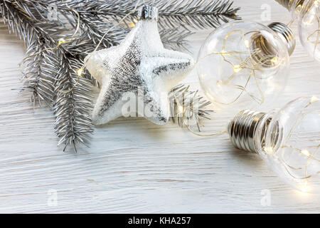silver christmas tree branch, decorations and glowing light lamps on white wooden background Stock Photo