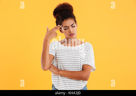 Young tired african lady making gun gesture with hand near head isolated over yellow Stock Photo