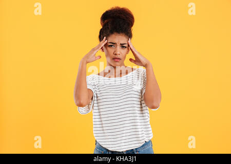 Young african ill tired woman holding her head while headache isolated over yellow Stock Photo