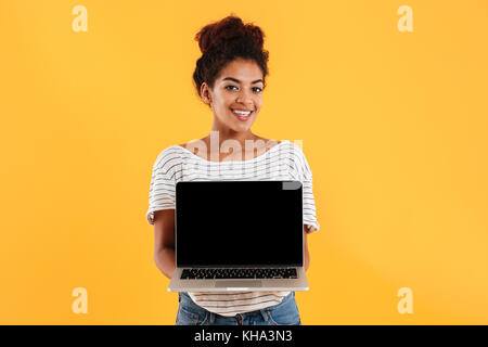 Young african beautiful lady with curly hair showing laptop computer with blank screen isolated Stock Photo