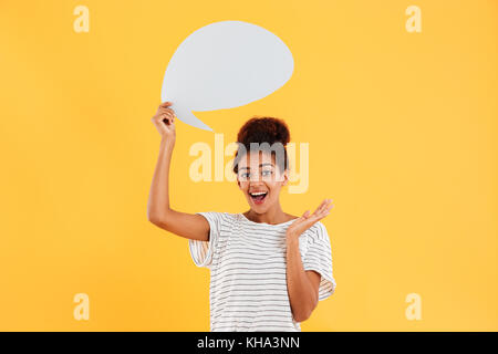 Young african happy lady looking camera and holding blank speech bubble isolated over yellow Stock Photo