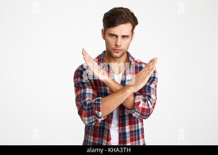 Close-up photo of serious handsome young man showing stop gesture with crossed hands, looking at camera, isolated on white background Stock Photo