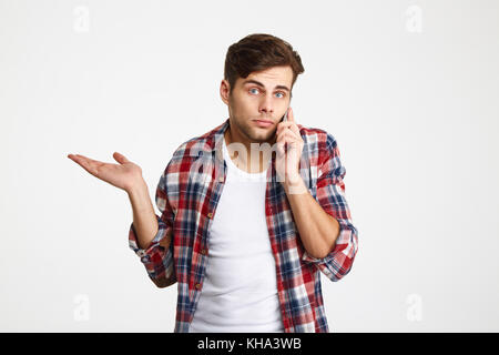 Portrait of a confused puzzled man talking on mobile phone isolated over white background Stock Photo