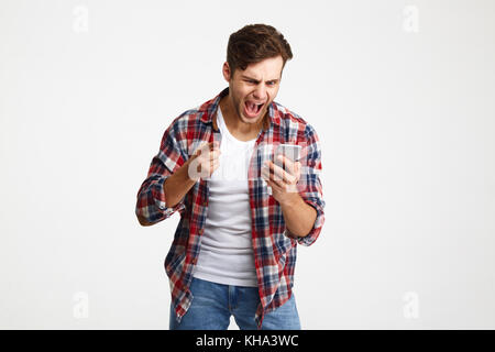Portrait of an angry unsatisfied man looking at mobile phone and yelling isolated over white background Stock Photo