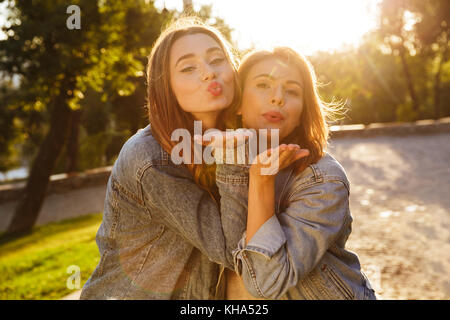 Portrait of two pretty young girls sending air kisses to camera while standing outdoors Stock Photo
