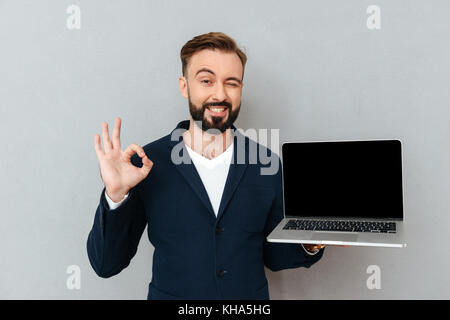 Young cheerful bearded man in suit looking camera while holding laptop computer isolated Stock Photo
