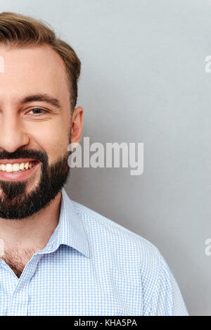 Vertical image of half face of smiling bearded man in business clothes looking at the camera over gary background Stock Photo