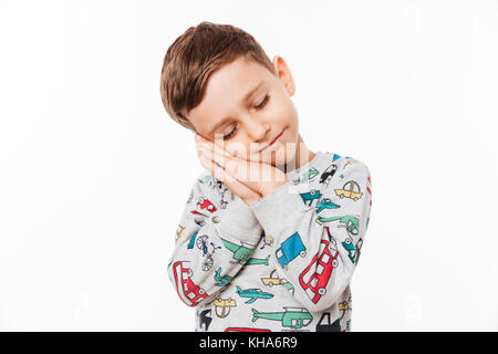 Portrait of a cute little kid standing with hands sealed pretending he is sleeping isolated over white background Stock Photo