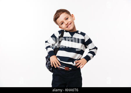 Portrait of a happy cute little kid with backpack standing with arms on hips and looking at camera isolated over white background Stock Photo