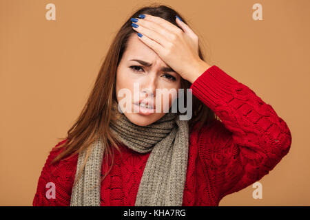 Close-up photo of unhealthy young caucasian woman touching her forehead, looking at camera, isolated on beige background Stock Photo
