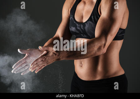 Cropped image of a muscular sportswoman clapping hands with talc powder before work out isolated over gray background Stock Photo