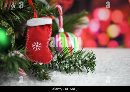 Warm cosy Christmas photography picture of little red stocking hanging on a tree with candy cane and stripe colourful bauble with snow and lights Stock Photo