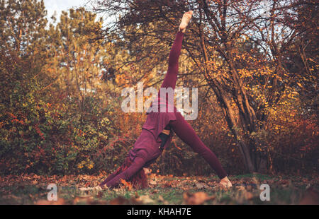 Girl on a bright autumn day practicing yoga outdoors, doing one-legged downward dog (eka pada adho mukha svanasana) Stock Photo