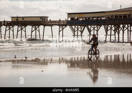 Bicycle rider on beach near pier with reflections. Stock Photo