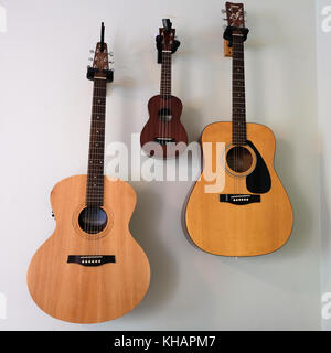 Two guitars and one banjo hanging on wall in symmetrical placement of musical instruments Stock Photo