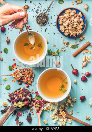 Two cups of healthy herbal tea with mint, cinnamon, dried rose, camomile flowers in spoons and man's hand holding spoon Stock Photo