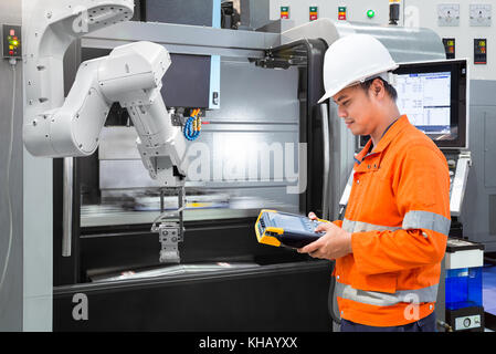 Maintenance engineer programming automatic robotic hand with CNC machine in smart factory. Industry 4.0 concept Stock Photo