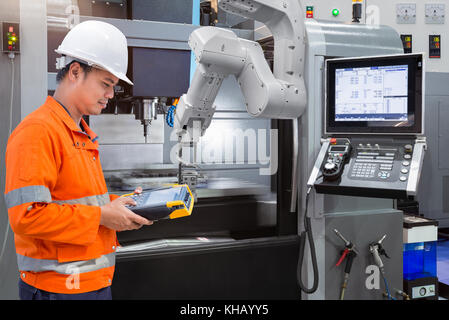 Maintenance engineer programming automatic robotic hand with CNC machine in smart factory. Industry 4.0 concept Stock Photo