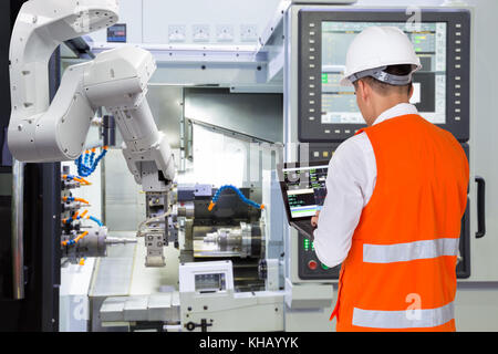 Engineer using laptop computer for maintenance automatic robotic arm with CNC machine in smart factory. Industry 4.0 concept Stock Photo