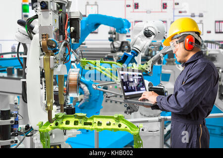 Engineer using laptop computer maintenance automatic robotic welding with robot workpiece in automotive industry, Smart factory concept Stock Photo