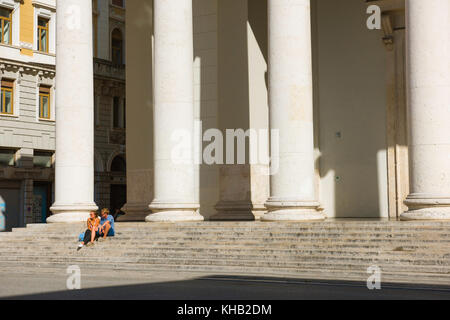 Young couple Italy, view of a young man and woman sitting alone on the steps of the Church of St Antony in the Piazza Sant'Antony Nuovo,Trieste, Italy. Stock Photo