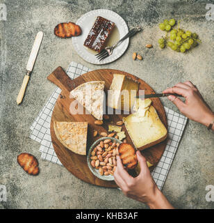 Cheese platter with female hands reaching to food, top view Stock Photo