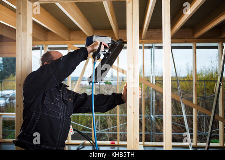 Mature carpenter drilling wood at construction site Stock Photo