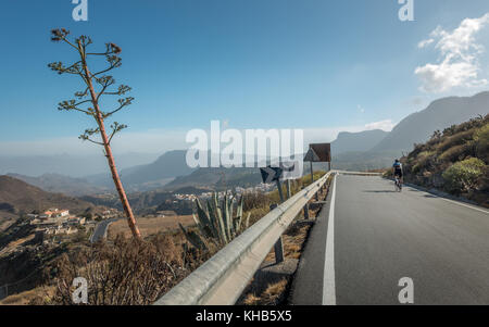 Cyclist cycling on a road bike with mountain views inland descending to San Bartolome on the GC-60 road, Gran Canaria Stock Photo