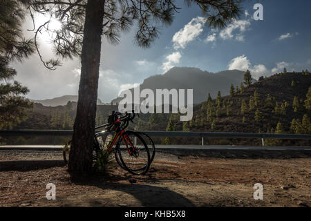 Mountain views inland with two bikes resting against a tree next to the road, Gran Canaria, Canary Islands Stock Photo