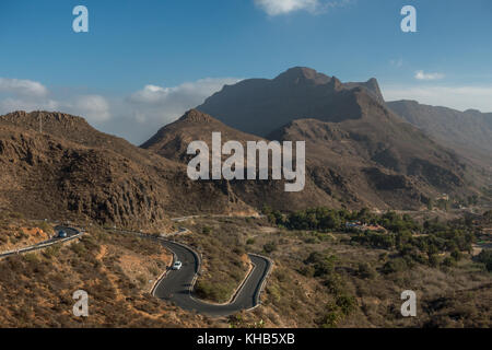 Car driving and cyclists cycling hairpin bends on road bikes with mountain views inland descending to Fataga on the GC-60 road, Gran Canaria Stock Photo