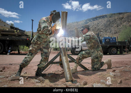 July 5, 2006 - Nogales, Arizona, USA - Arizona Army National Guard specialist Ruben Cordova, left welds together a vehicle barrier while Sgt. first class Gustavo Dagino holds the pieces in place near the US-Mexico border in Nogales, Ariz., July 5, 2006. The used railroad rails prevent vehicles of human and drug smugglers from driving vehicles across the border. Part of the border fence is visible in the background. Arizona has deployed 300 members along the state's international border as a part of Operation Jump Start, the federal effort to use guard members to do non-partol jobs, relieve bor Stock Photo