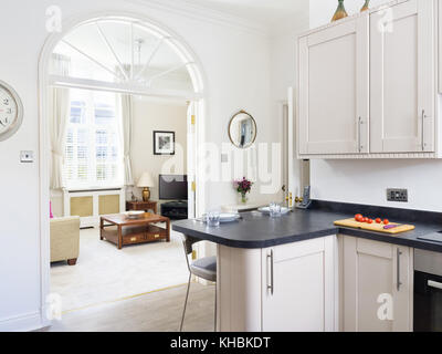 A fresh, light, traditional yet contemporary kitchen. furnished with fitted cabinets & a breakfast bar. With a view in to a living room. Stock Photo