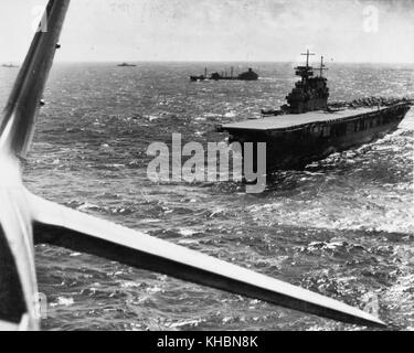 The U.S. Navy aircraft carrier USS Yorktown (CV-5) operating in the Pacific in February 1942, photographed from a Douglas TBD-1 torpedo plane that has just taken off from her deck. Other TBD and SBD aircraft are also ready to be launched. A F4F-3 'Wildcat' fighter is parked on the outrigger just forward of the island. The other ships in company include the fleet oiler USS Guadaloupe (AO-32), a destroyer and a heavy cruiser. Stock Photo
