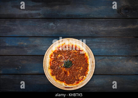 Delicious pizza with minced meat on a wooden stand on a dark wooden background. Top view bottom orientation. Stock Photo