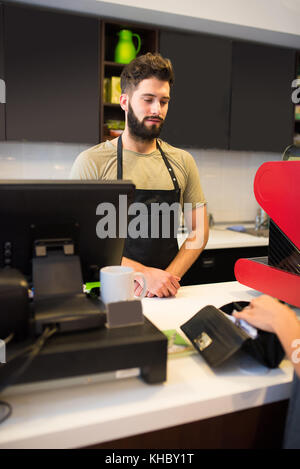 Two beautiful young woman buying coffee in a coffee shop from a barista guy Stock Photo