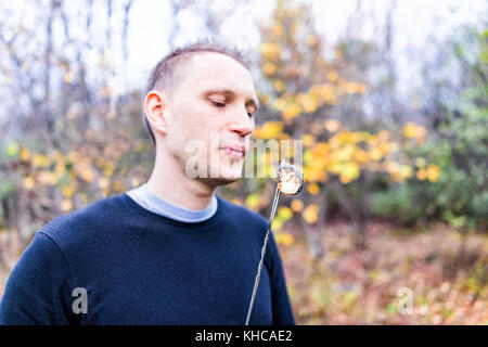 Young man blowing on roasted caramelized marshmallow skewer to cool it off closeup portrait in nature, camping on campground Stock Photo
