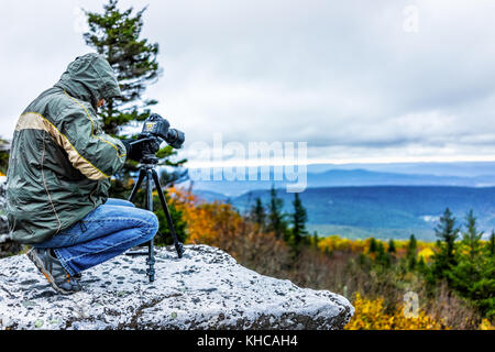 Standing young man photographer with camera, gear and tripod on cold autumn morning in jacket in Bear Rocks, West Virginia taking pictures of sunrise Stock Photo