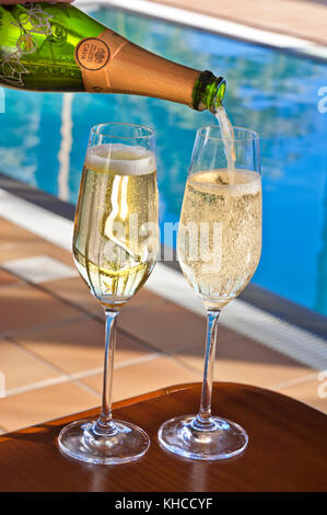 CAVA SPAIN LUXURY POOL Pouring glasses of sparkling Spanish Cava wine in sunny vacation  luxury Hotel Villa infinity swimming pool poolside setting Stock Photo
