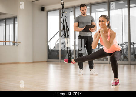 Young adult girl doing suspension rope exercise together with her personal private coach. Stock Photo