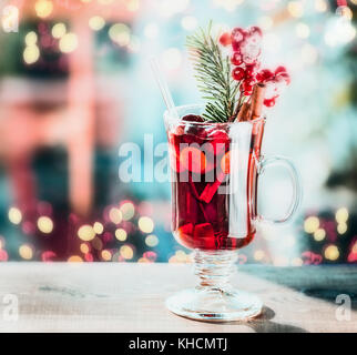 Glass of spiced mulled wine with berries and fir branch on table at festive bokeh lighting background Stock Photo