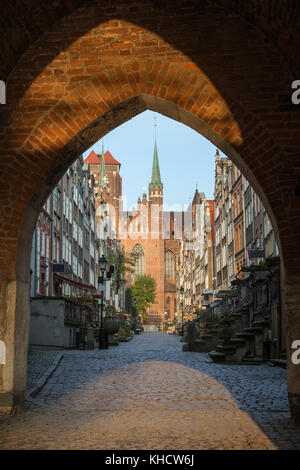 Old buildings on the St. Mary's Street and St. Mary's Church at the Main Town (Old Town) in Gdansk, viewed through an arched gateway in the morning. Stock Photo