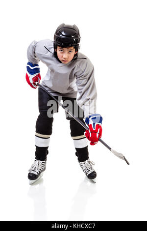 Portrait of junior ice hockey player on the alert with full equipment and uniform posing for a shot with a puck. Isolated on white background. Stock Photo