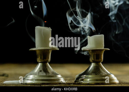 Blown candles in silver candlesticks with smoked wick. Smoke from a wick on a black background. Wooden table Stock Photo