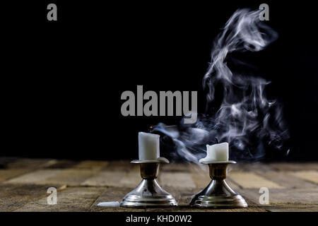 Blown candles in silver candlesticks with smoked wick. Smoke from a wick on a black background. Wooden table Stock Photo