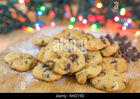 Freshly baked chocolate chip cookies on wooden board with colored lights in background, selective focus Stock Photo