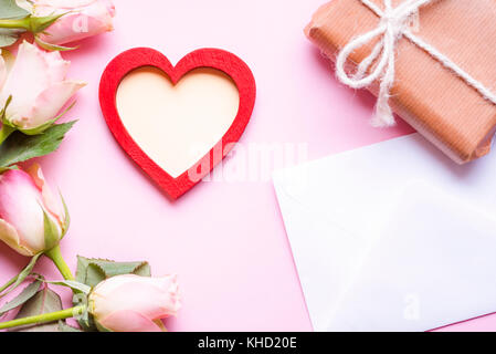 Valentine day theme image with a red heart with copy space in the middle, surrounded by pink roses, an envelope and a gift wrapped in brown paper, on  Stock Photo