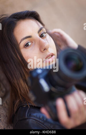 Young Adult Ethnic Female Photographer Against Wall Holding Camera. Stock Photo