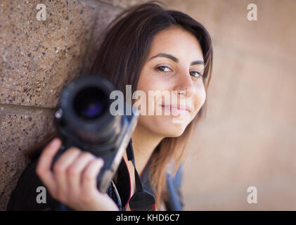 Young Adult Ethnic Female Photographer Against Wall Holding Camera. Stock Photo