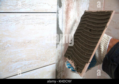 industrial construction worker installing small ceramic tiles on bathroom walls and applying mortar with trowel Stock Photo